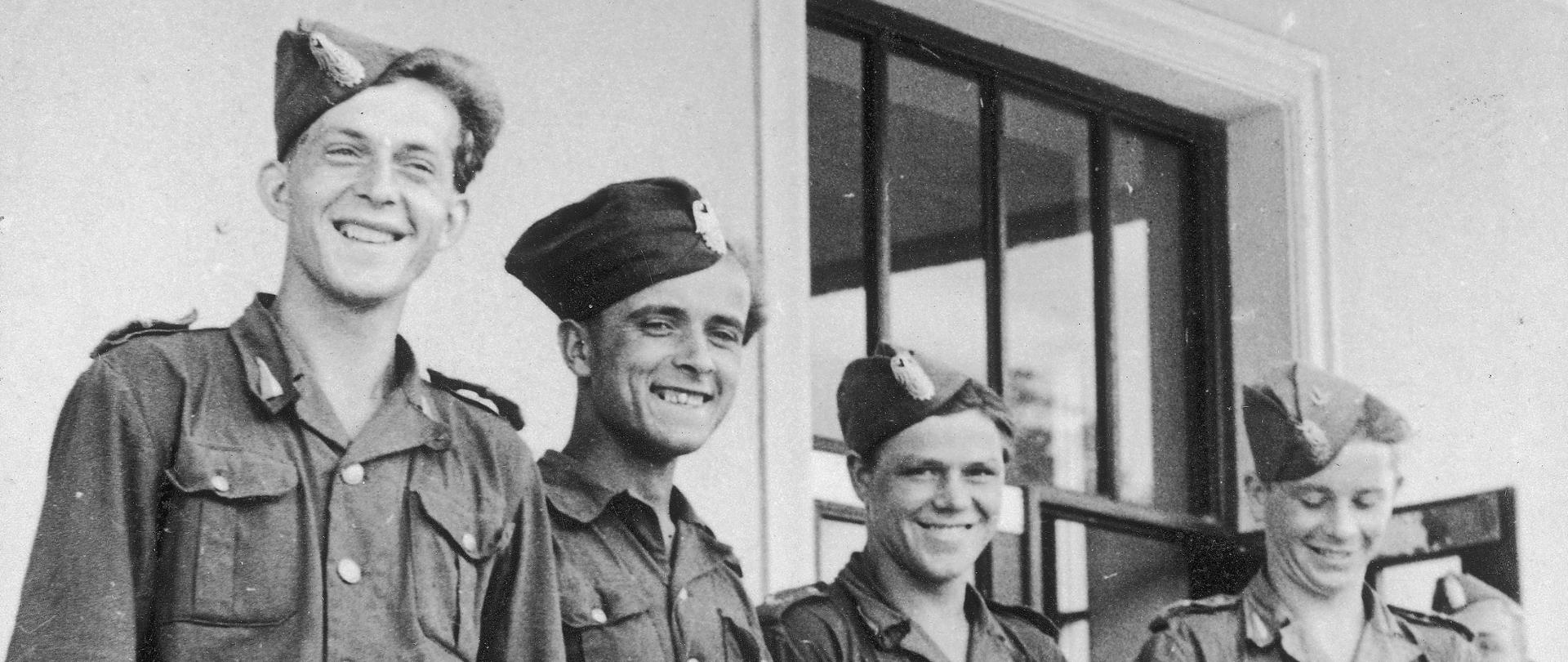 Czterech młodych mężczyzn w mundurach junackich, na głowach mają zawadiacko ubrane furażerki (czapki wojskowe). Mężczyźni trzymają w dłoniach dyplomy, uśmiechają się.
