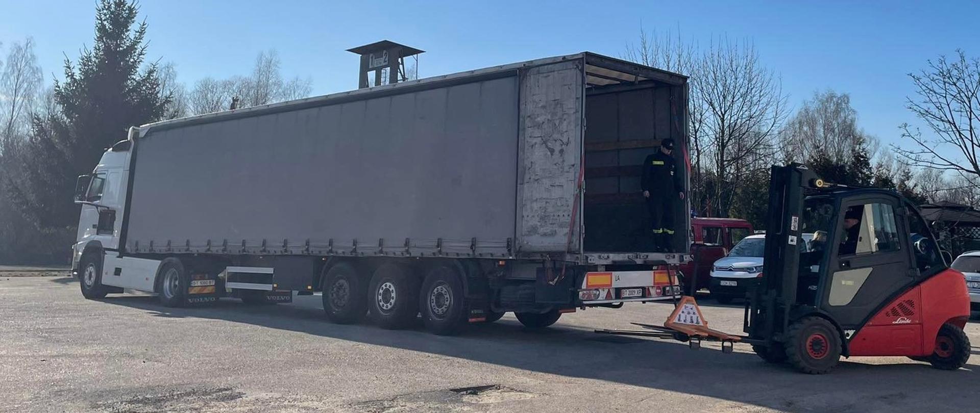 Na zdjęciu znajduje się TIR podczas załadunku na terenie Komendy Powiatowej PSP w Chełmnie. Palety ładowane są wózkiem widłowym przez funkcjonariusza komendy.