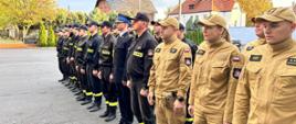 Strażacy stoją podczas zbiórki, przed budynkiem komendy.