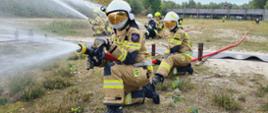 Grupa osób w ubraniach specjalnych straży pożarnej podaje prądy gaśnicze