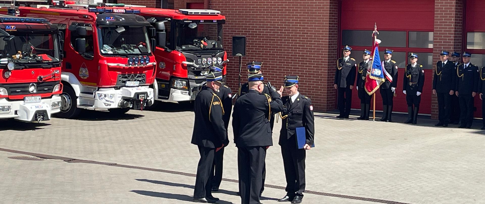 Komendant wręcza awanse strażakom. W tyle pozostali strażacy stojący w dwuszeregu wraz z pocztem sztandarowym
