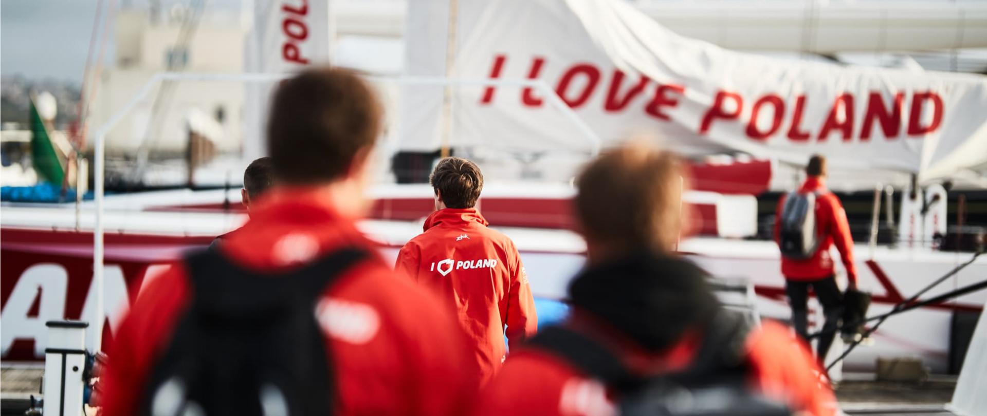 Młodzi żeglarze zmierzający w stronę statków. Napis I LOVE POLAND na kurtce jednego z nich.