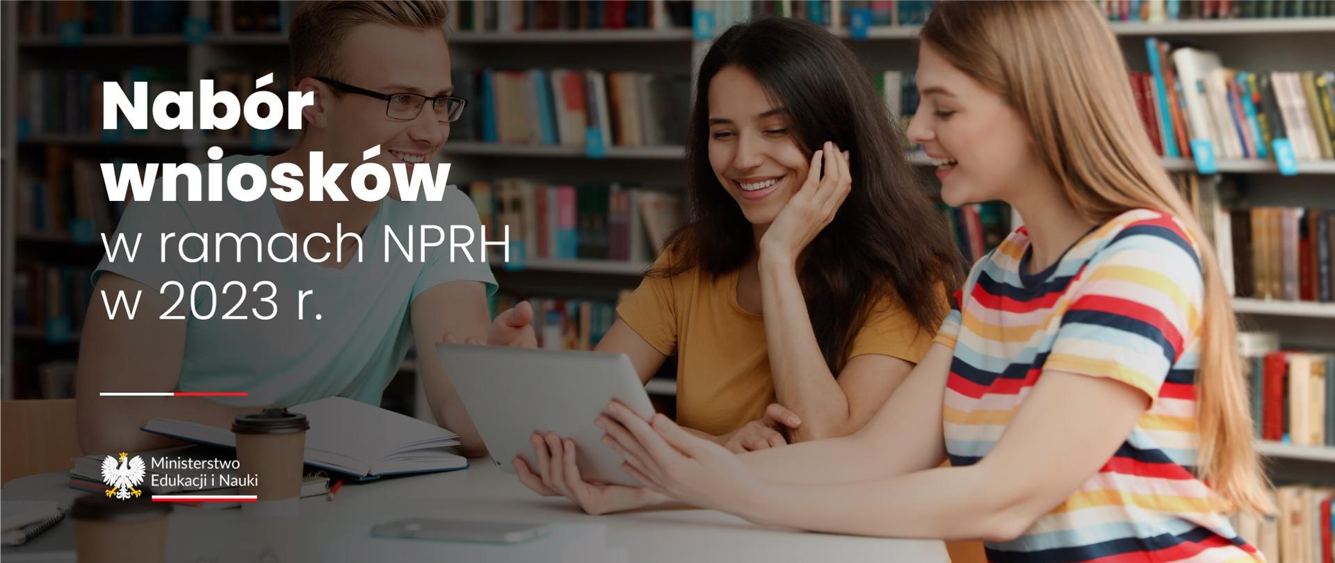 Kilkoro młodych ludzi siedzi w bibliotece nad laptopem, obok napis Nabór wniosków w ramach NPRH w 2023 r.