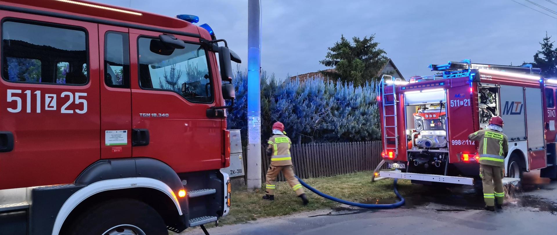 Dwa samochody ratowniczo- gaśnicze. Strażak tankuje wodę do jednego z pojazdów.