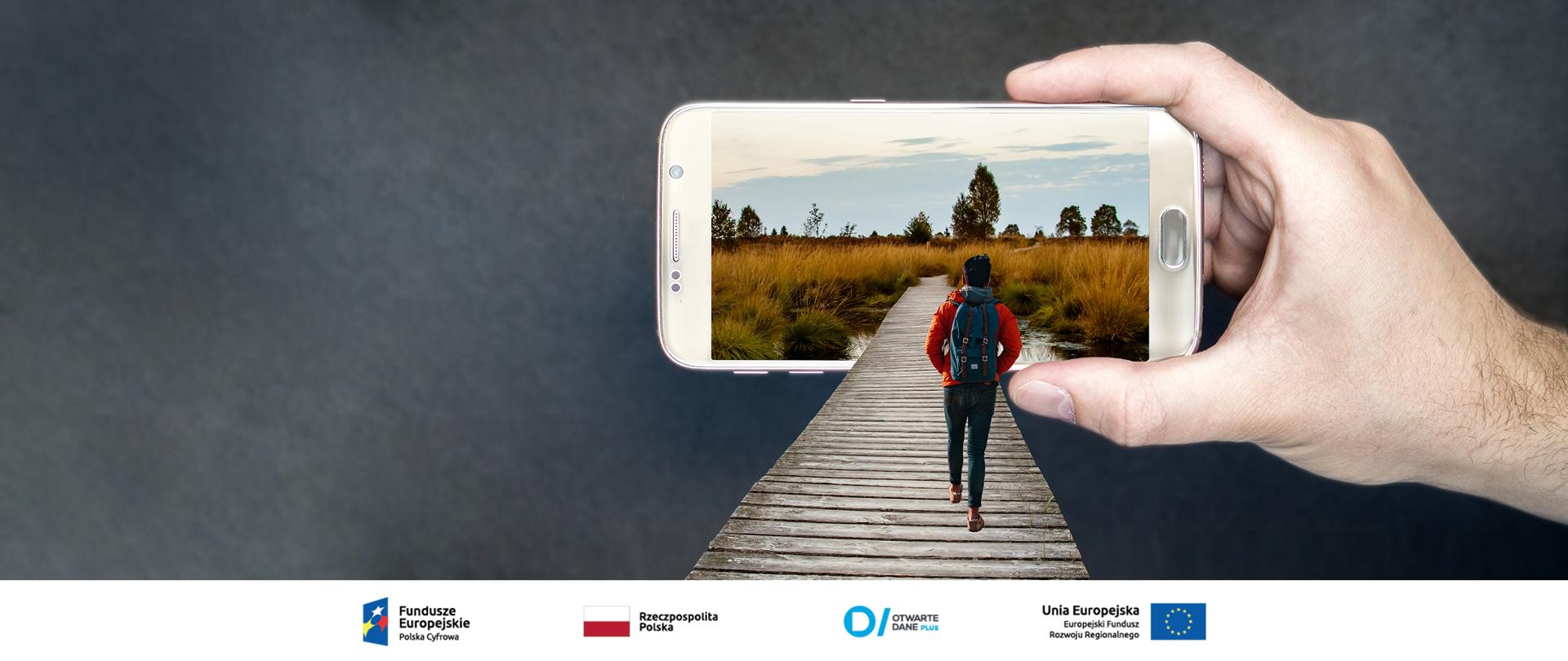 Grafika. Mężczyzna z plecakiem idzie pomostem w stronę smartfona z widokiem łąki. 