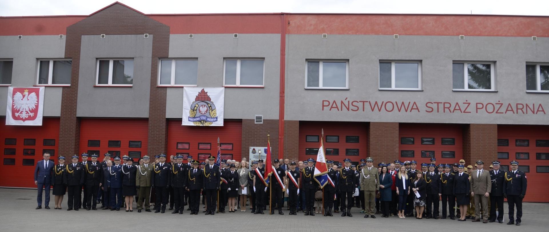 Na zdjęciu widać budynek Komendy Miejskiej Państwowej Straży Pożarnej w Piekarach Śląskich, poczty sztandarowe, funkcjonariuszy, pracowników cywilnych i zaproszonych gości