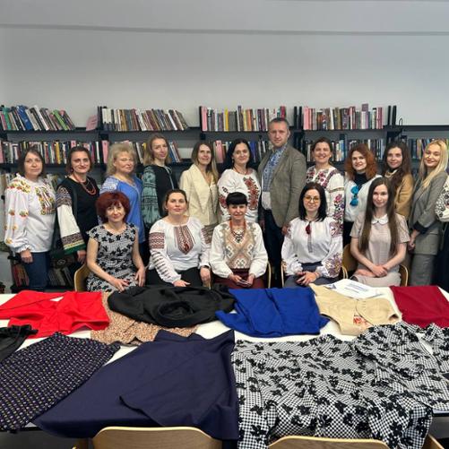 Grupa kobiet i mężczyzna pozują do zdjęcia przed stołem, na którym rozłożone są ubrania