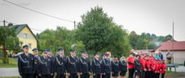 Na zdjęciu widoczni strażacy OSP w ubraniach galowych koloru granatowego stojący w pododdziale podczas uroczystego apelu z okazji przekazania samochodu ratowniczo-gaśniczego dla OSP Smerekowiec