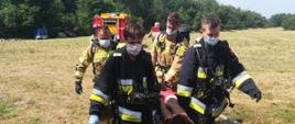 Zdjęcie przedstawia strażaków którzy niosą osobę poszkodowaną na noszach typu deska.