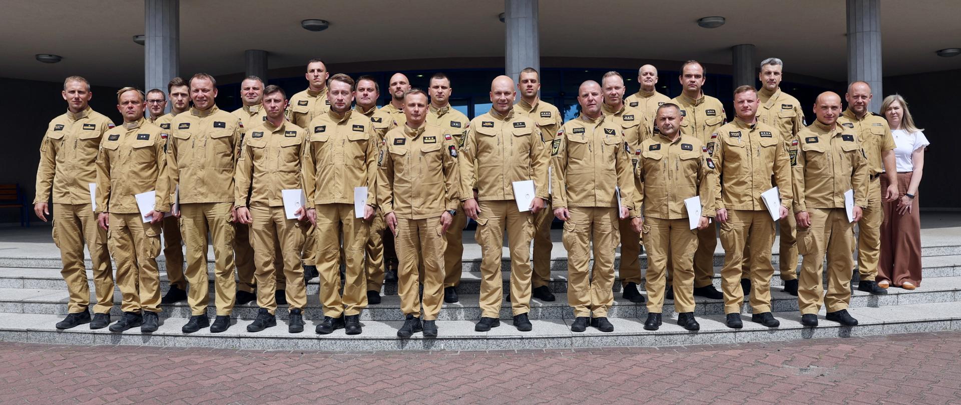 Pamiątkowe zdjęcie grupowe funkcjonariuszy PSP uczestniczących w szkoleniu z zakresu kierowania działaniem ratowniczym na poziomie interwencyjnym (20 osób) w towarzystwie Zastępcy Komendanta Centralnej Szkoły PSP, kobiety oraz trzech funkcjonariuszy CS PSP