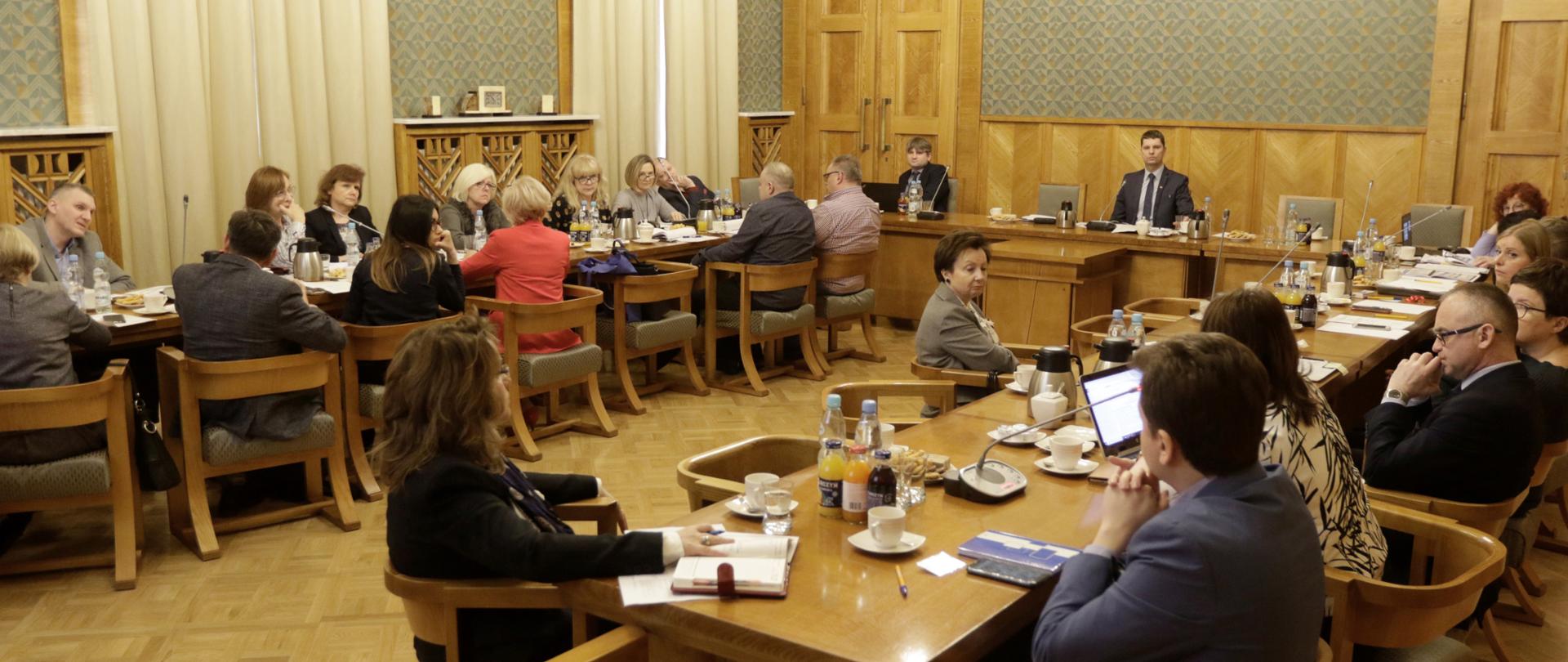 Posiedzenie Zespołu do spraw statusu zawodowego pracowników oświaty. Uczestnicy siedzą na sali obrad. Na środku sali za stołem siedzi minister edukacji.