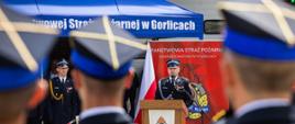 Na zdjęciu widoczny pododdział od tyłu oraz przemawiający prezes powiatowy Związku Ochotniczych Straży Pożarnych Rzeczypospolitej Polskiej w Gorlicach podczas obchodów powiatowych dnia strażaka w Gorlicach. W tle widoczny niebieski namiot i rolap a na czerwonym tle napis koloru białego Państwowa Straż Pożarna Komenda Powiatowa Państwowej Straży Pożarnej w Gorlicach a obok flagi biało czerwone.