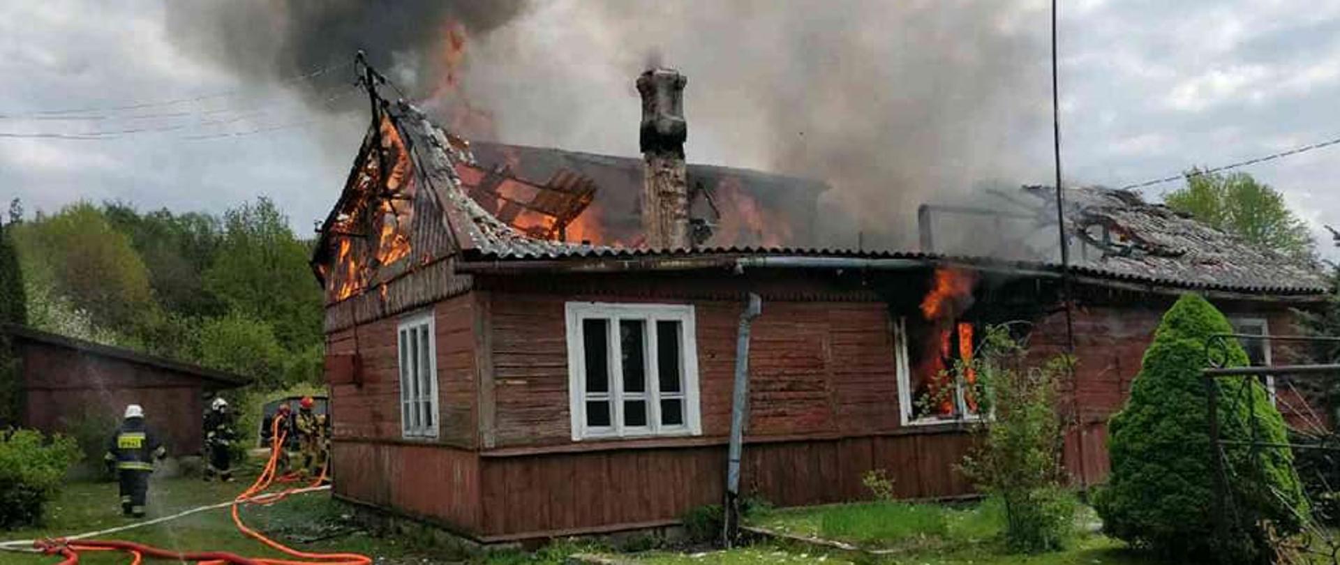 strażacy prowadzą działania gaśnicze, budynek cały w ogniu, częściowo zawalony dach.