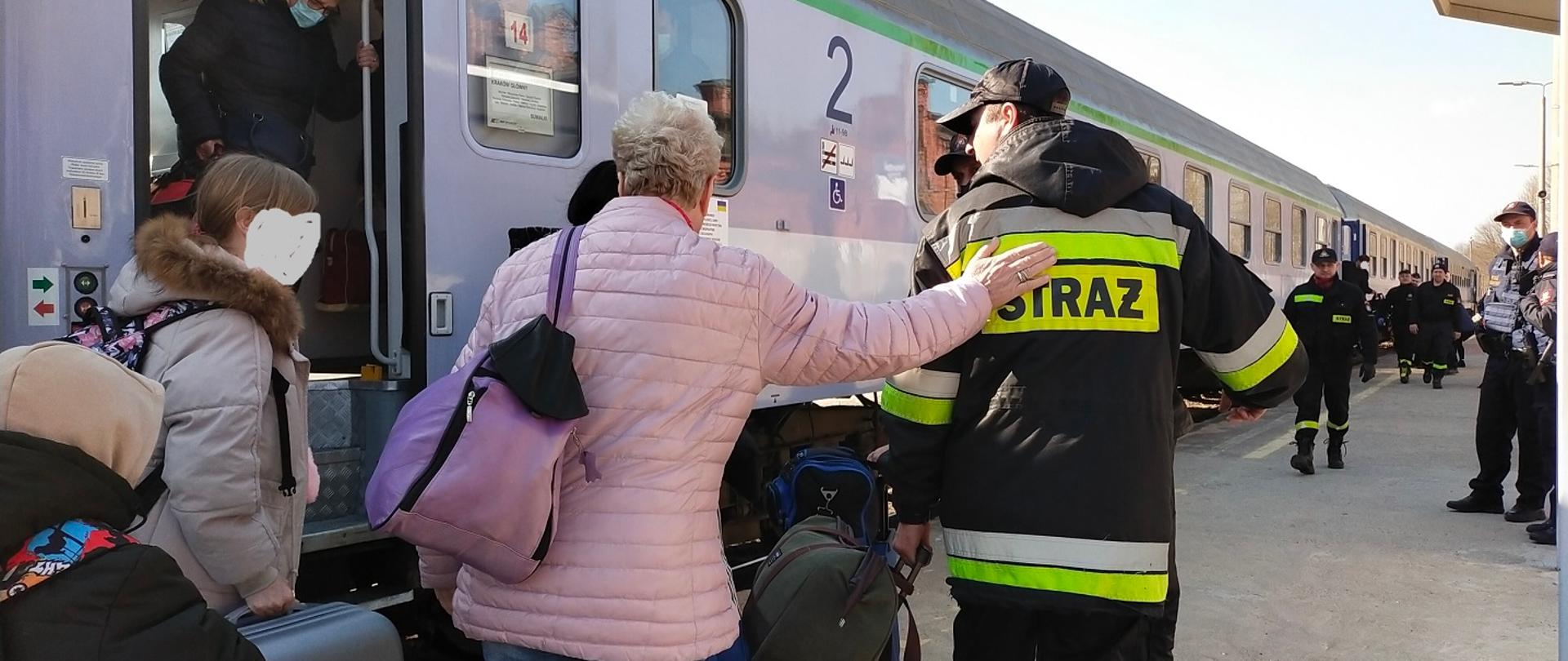 Zdjęcie obrazuje ludzi na peronach i wysiadających z pociągu oraz pomagających im strażaków 