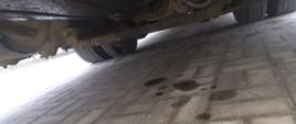 Podwozie autobusu szkolnego z widocznymi śladami wycieku oleju napędowego. Na kostce betonowej pod pojazdem są widoczne spore plamy oleju.