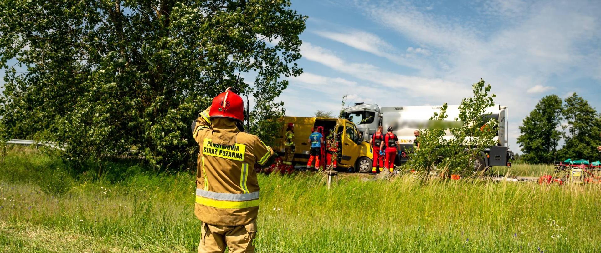 Dowódca kontaktuje się za pomocą łączności bezprzewodowej ze stanowiskiem kierowania, w tle akcja ratunkowa