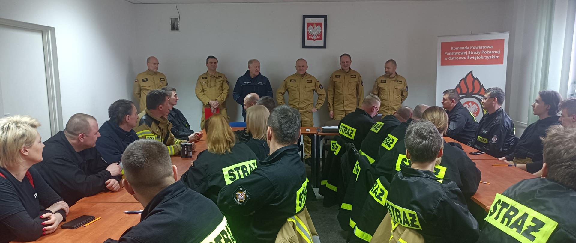 Na zdjęciu widać przedstawicieli KP PSP w Ostrowcu Św., którzy stoją w pomieszczeniu komendy i przemawiają do przyszłych ratowników - druhów OSP.
