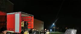 wieczór, na sużym placu strażacy pakuja do samochodu duże palety owinięte czarnym streczem