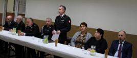 Komendant Powiatowy PSP Skarżysko-Kamienna przemawia podczas zebrania sprawozdawczego w OSP Nowy Odrowążek. Po jego lewej jak i prawej stronie siedzą włodarze gminy, poseł RP, wicestarosta.