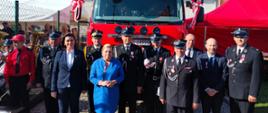 Goście uczestniczący w uroczystości, w tle czerwony samochód pożarniczy