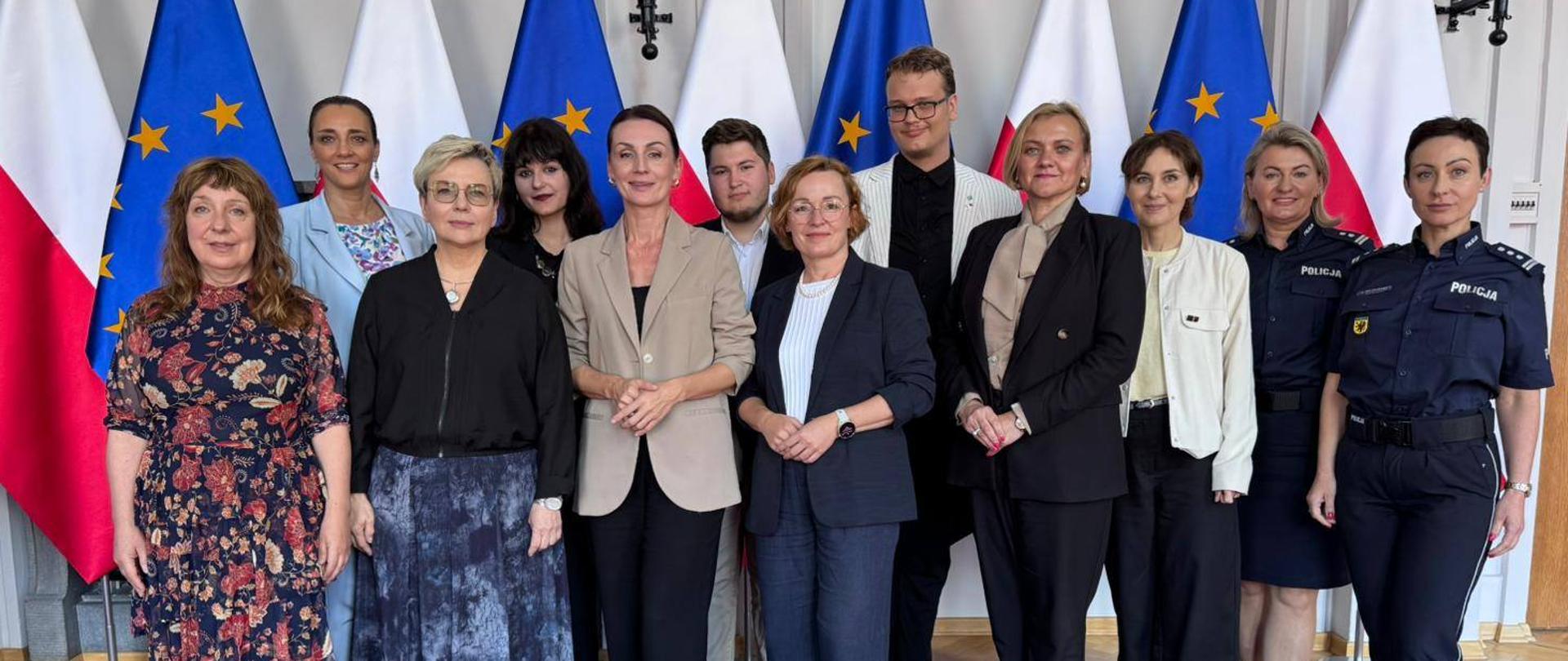 grupa osób pozuje do zdjęcia na tle biąło - czerwonych flag