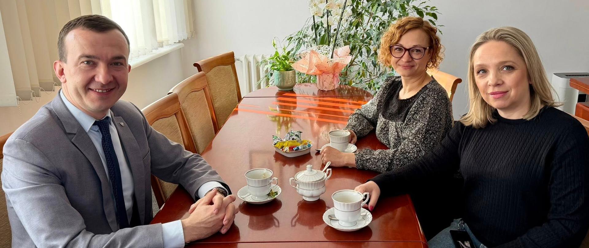 Mężczyzna i 2 kobiety siedzą przy stole 