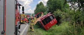 Zdjęcie przedstawia przewróconego busa który leży w rowie. Obok znajdują się zastępy straży pożarnej oraz Pogotowie Ratunkowe