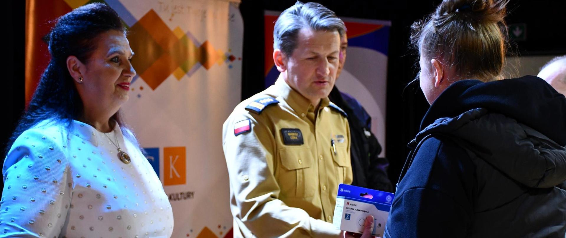 Fotografia przedstawia burmistrza gminy Piekoszów i komendanta miejskiego PSP w Kielcach podczas wręczania czujek dymu i tlenku węgla.