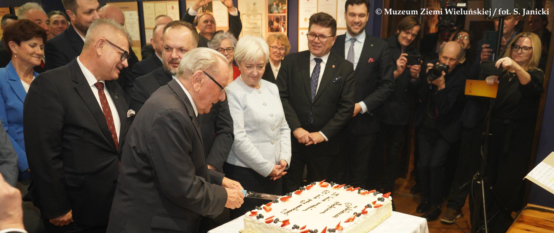 Jubilat wraz z zaproszonymi gośćmi, podczas krojenia tortu 