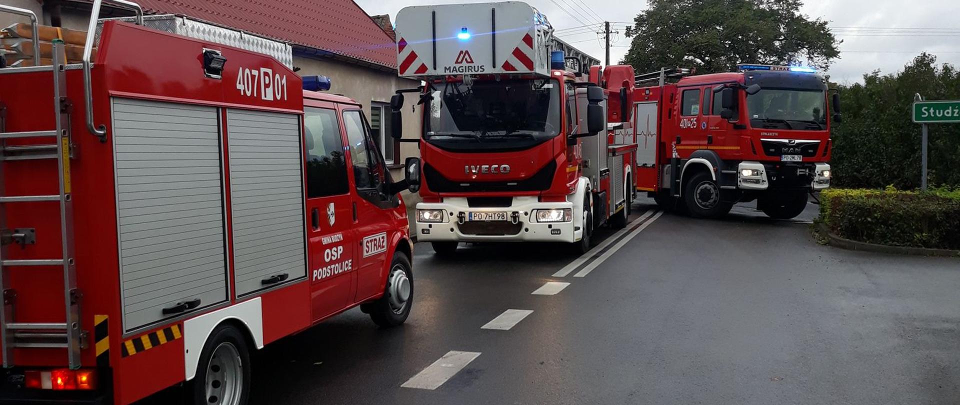 Przy budynku jednorodzinnym stoją 3 pojazdy strażackie w trakcie gaszenia pożaru w kotłowni w piwnicy budynku jednorodzinnego w Podstolicach. 