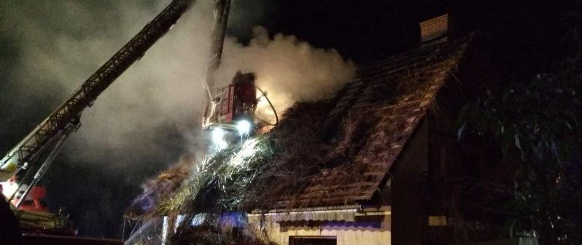 Pożar domu jednorodzinnego, pokrytego strzechą, w Dębiankach. Strażacy prowadzą działania z podnośnika SH23.