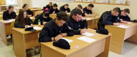 Widok z boku. Uczestnicy szkolenia w trakcie egzaminu pisemnego na sali szkoleniowej JRG.