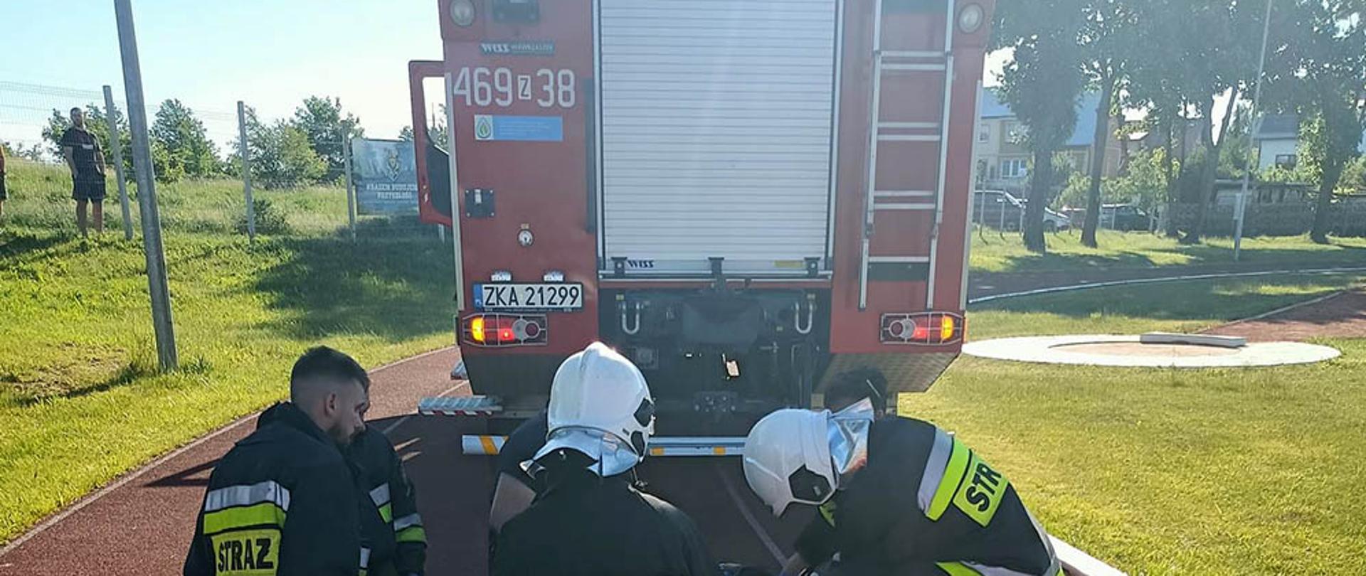 Zdjęcie przedstawia 34 strażaków ochotników udzielających pomocy poszkodowanemu na boisku.w tle widać samochód.