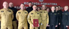 Zdjęcie grupowe osób biorących udział w spotkaniu, na którym wręczono strażakowi decyzję o powołaniu na stanowisko technika w wydziale operacyjno-szkoleniowym