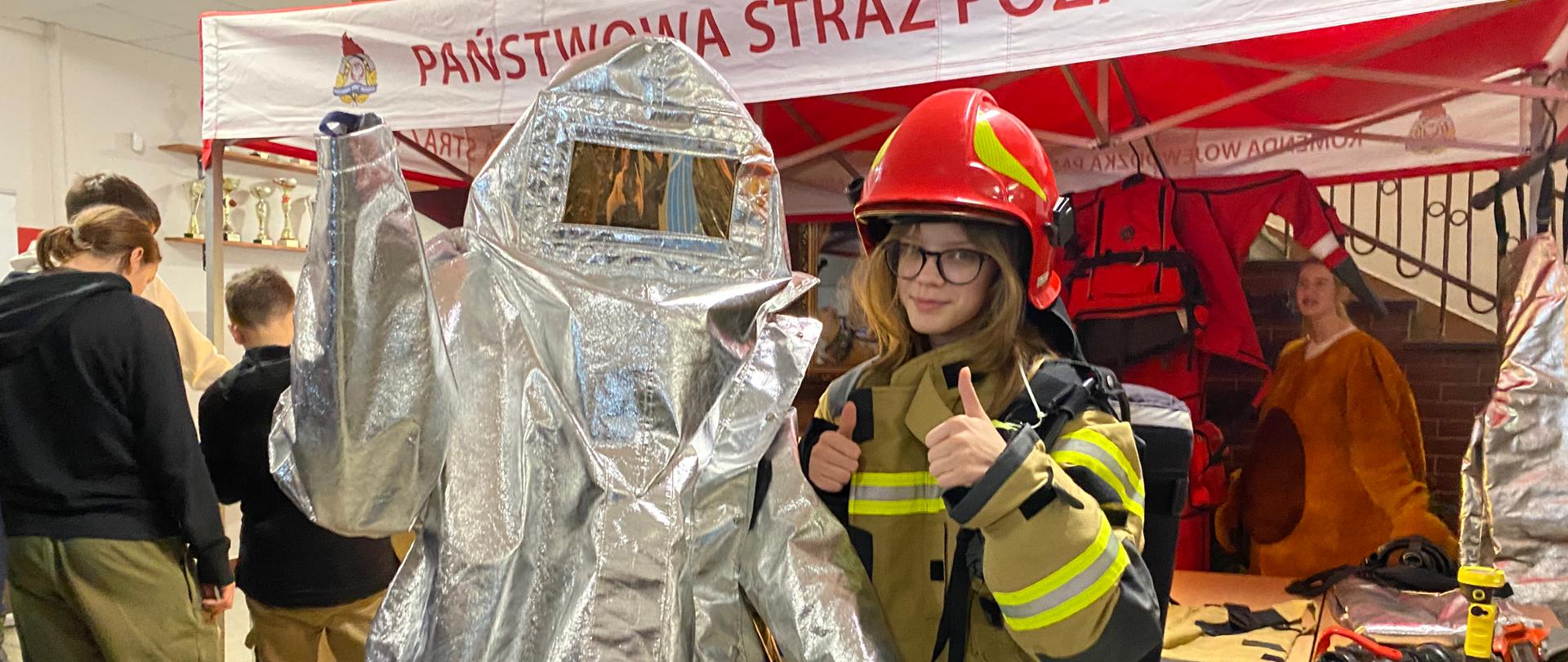 Dwie dziewczyny przebrane w mundury - bojowy i specjalny. W tle stoisko PSP. Widać też innych zwiedzających.