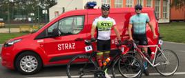 Dwóch zawodników stoi z rowerami na tle samochodu strażackiego.