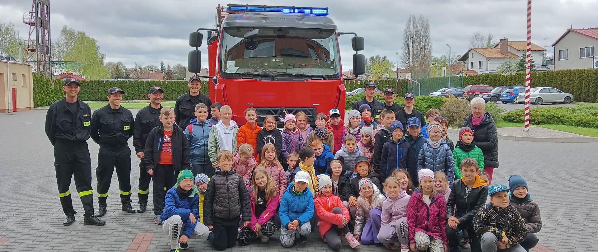 Zdjęcie przedstawia strażaków i uczniów oraz nauczycieli pozujących razem na tle samochodu strażackiego.