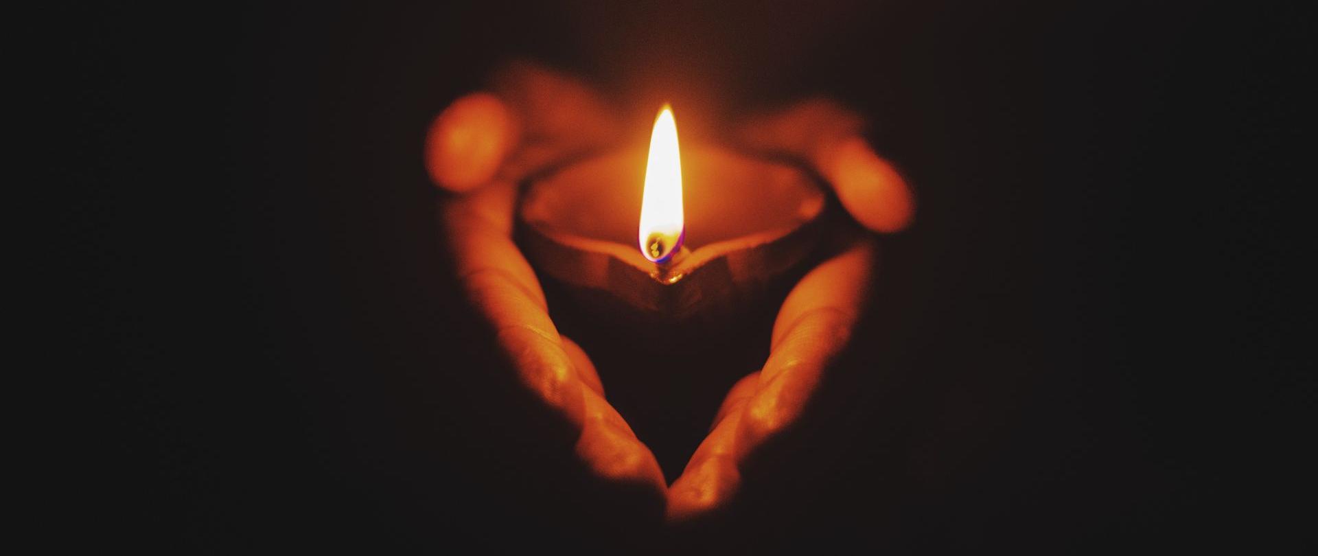 zapalony kaganek niesiony w złączonych dłoniach