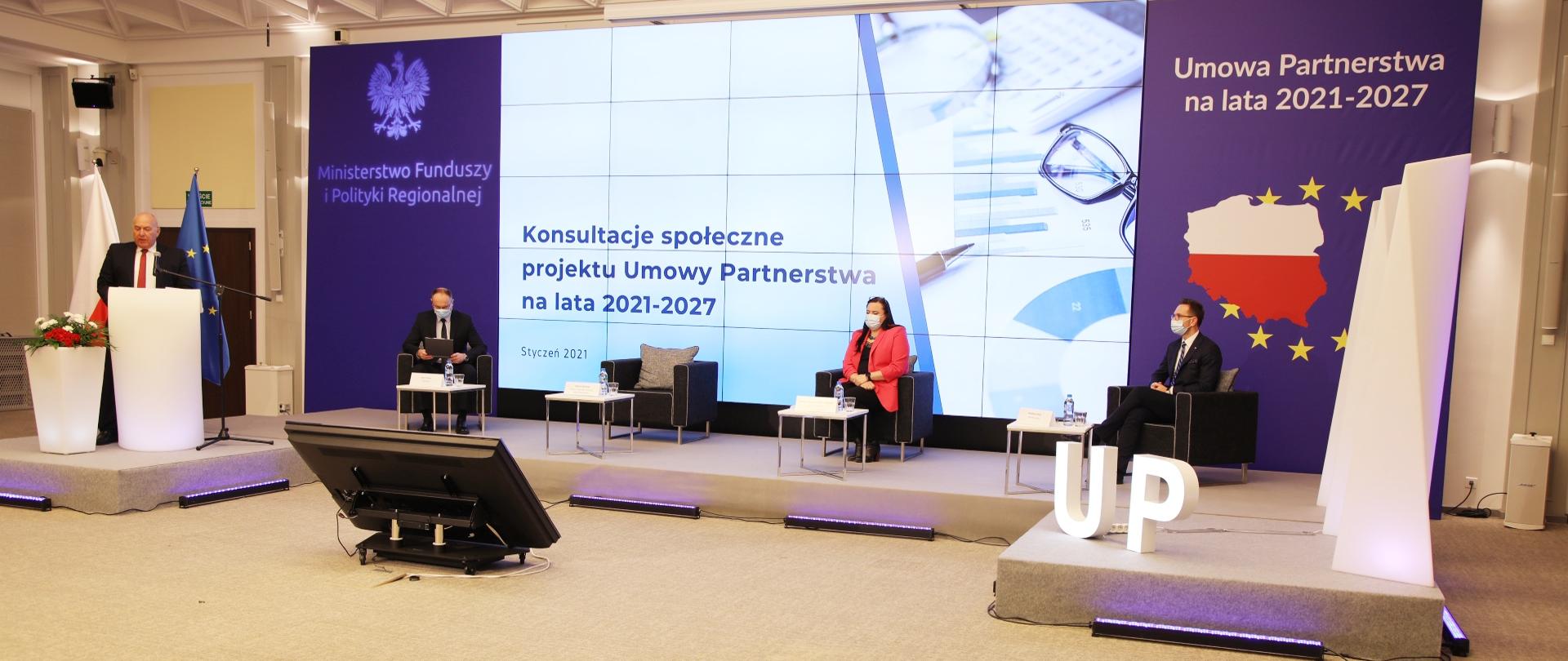 W sali konferencyjnej na podeście trzy osoby siedzą w fotelach przed stolikami. Od prawej wiceministrowie Waldemar Buda i Małgorzata Jarosińska-Jedynak oraz prowadzący spotkanie. Od lewej w mównicy stoi minister Tadeusz Kościński.