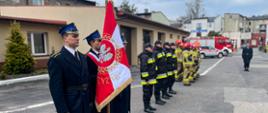 Zdjęcie zrobione na placu komendy, ukazuje strażaków ustawionych w jednym rzędzie podczas uroczystej zbiórki w mundurach wyjściowych, służbowych i specjalnych.