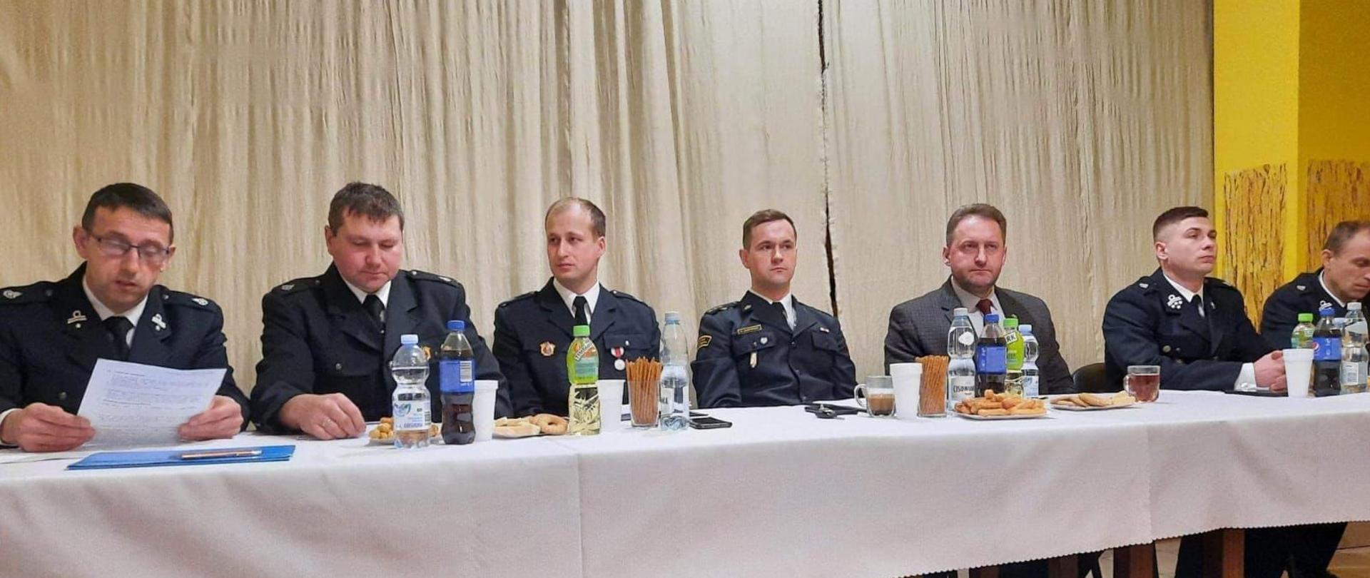 Zdjęcie przedstawia stół prezydialny za którym siedzą organizatorzy oraz zaproszeni goście na spotkanie noworoczne Ochotniczej Straży Pożarnej we Wzdole Rządowym.