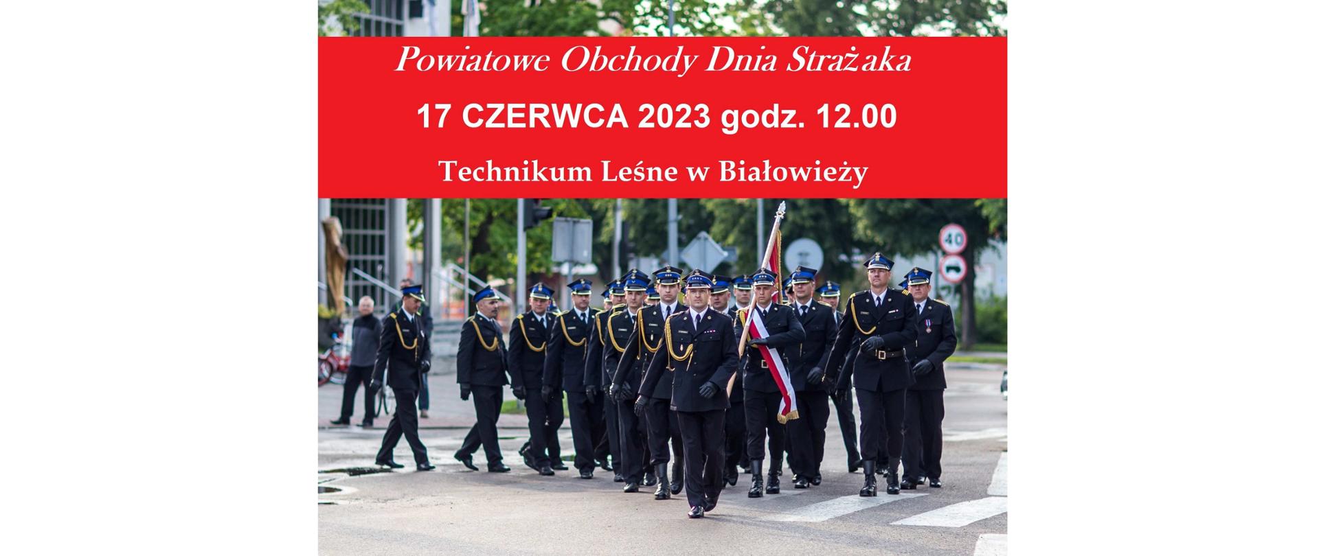 Po ulicy maszeruje pododdział strażaków ze sztandarem.