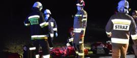 Wypadek w Stwolnie. Na jezdni - na desce ortopedycznej leży ranna kobieta, wcześniej zaopatrzona przez strażaków. Wokół niej pięciu strażaków, z których jeden klęczy przy poszkodowanej. Z przodu i z tyłu poszkodowanej stoją torby i sprzęt medyczny.