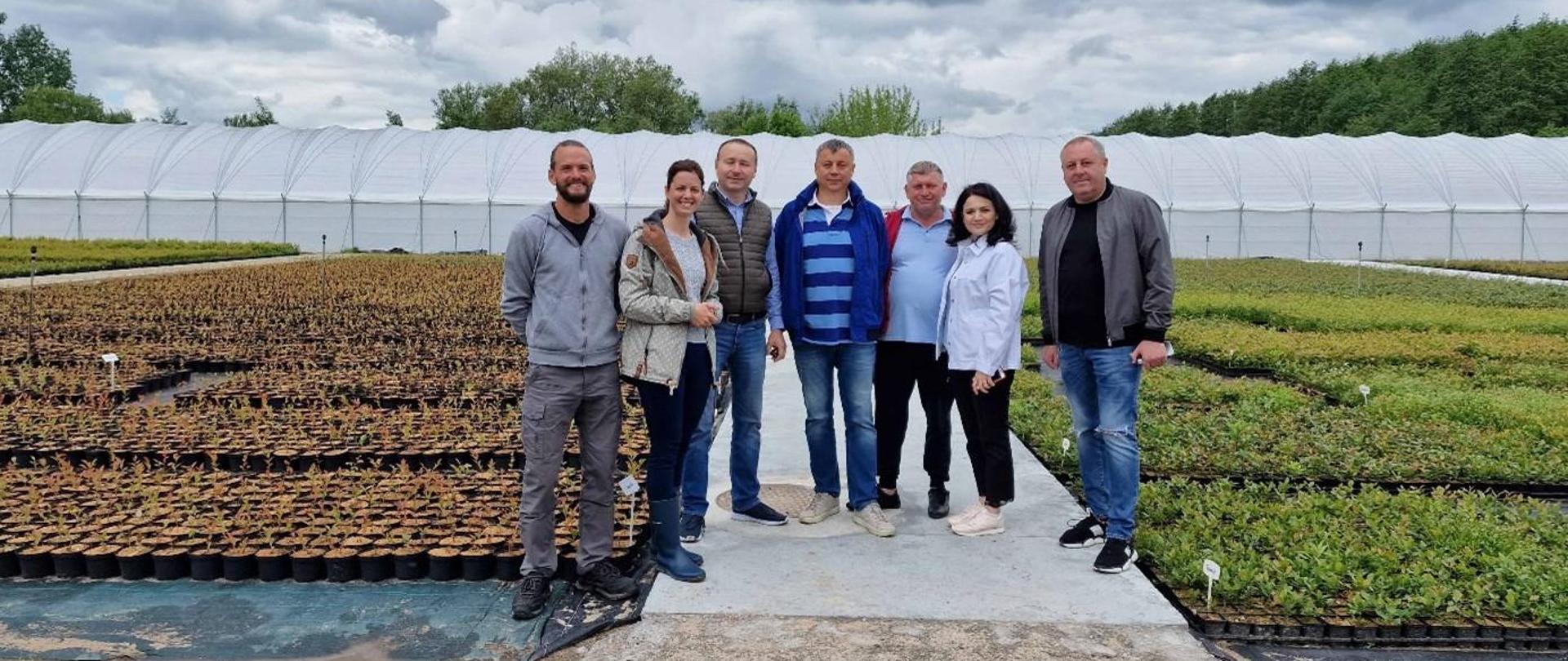 Grupa 7-osobowa pozuje do zdjęcia na plantacji, w tle duży rolniczy tunel foliowy.