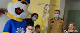 Na zdjęciu znajduje się policjantka, strażak oraz kobieta i dzieci pacjenci oddziału pediatrii i maskotka policjanta "Poluś"