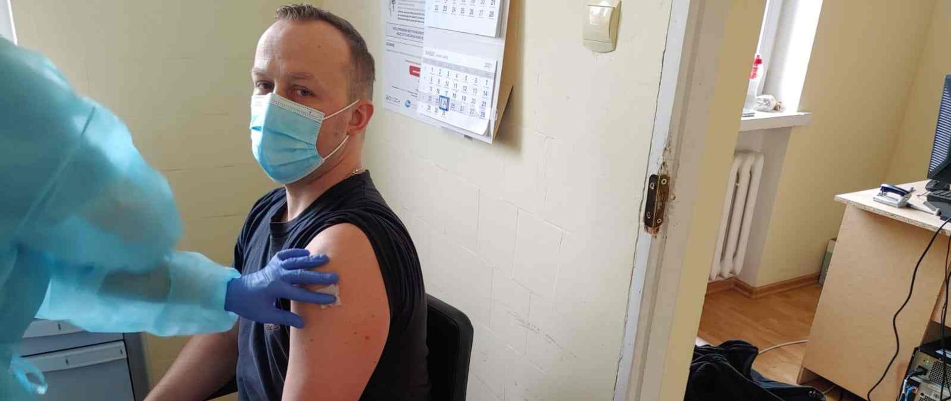 Strażak siedzący w punkcie szczepień chwilę po zaszczepieniu.