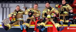 Na zdjęciu czterech strażaków siedzących na podeście samochodu – drabiny pożarniczej. Strażacy ubraniach specjalnych (nomexach), każdy z nich ma na stopach dwie inne, różnokolorowe skarpetki.