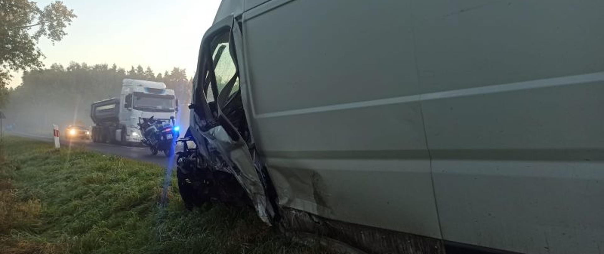 Widok na miejsce zdarzenia. Z prawej strony widać uszkodzony bok białego auta dostawczego. Z oddali las i nisko unosząca się mgła.