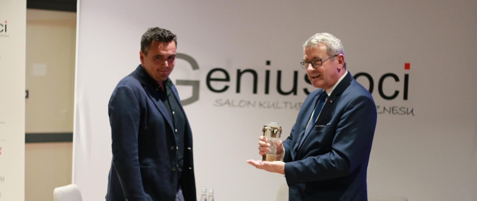 Minister Murdzek wręcza nagrodę - statuetkę, w tle ściana z napisem Genius Loci.