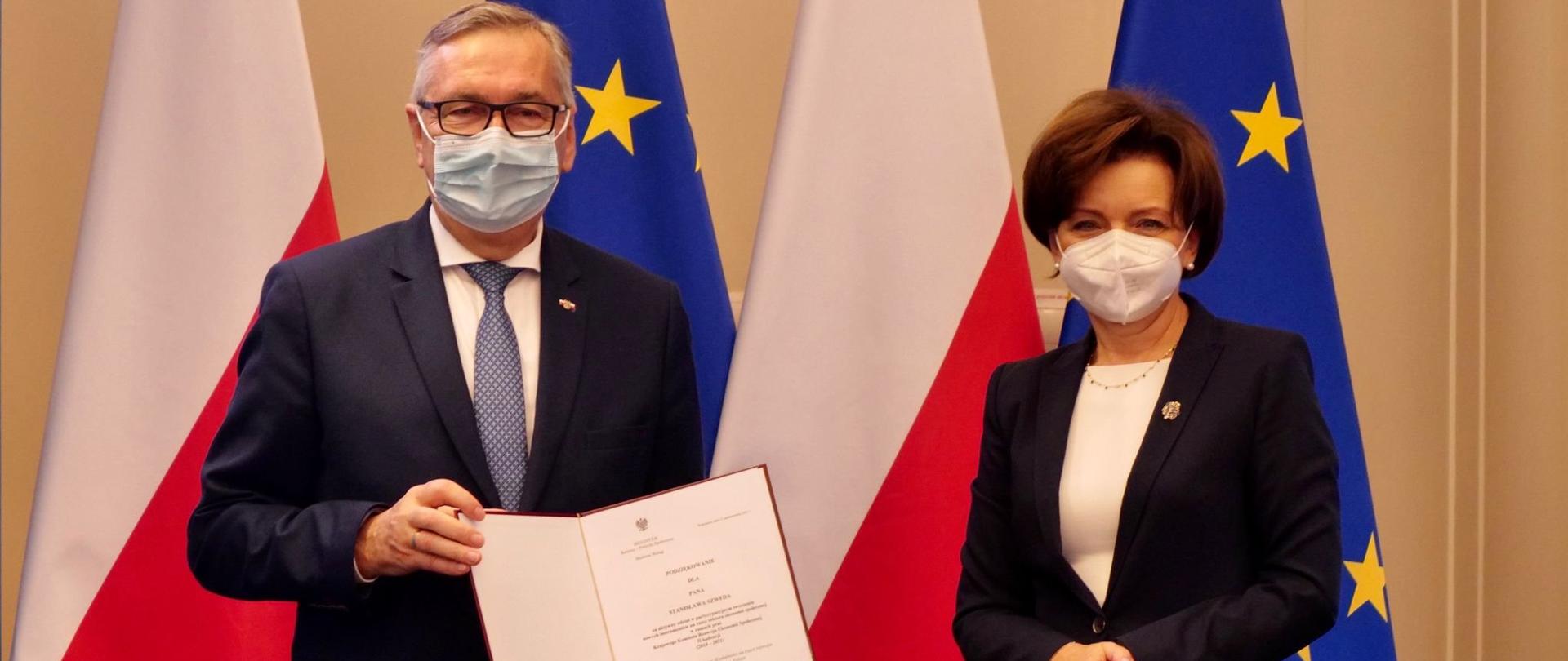 Na zdjęciu stoją obok siebie minister Maląg oraz wiceminister Szwed. W tle flagi Polski i unijne.